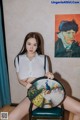 A woman sitting on a chair holding a painting of a peacock.