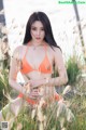 A woman in an orange bikini sitting in tall grass.