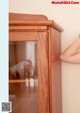 A woman leaning against a wooden cabinet with a glass door.