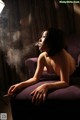 A naked woman sitting on a purple couch smoking a cigarette.