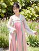 A woman in a pink and white hanbok standing in a garden.